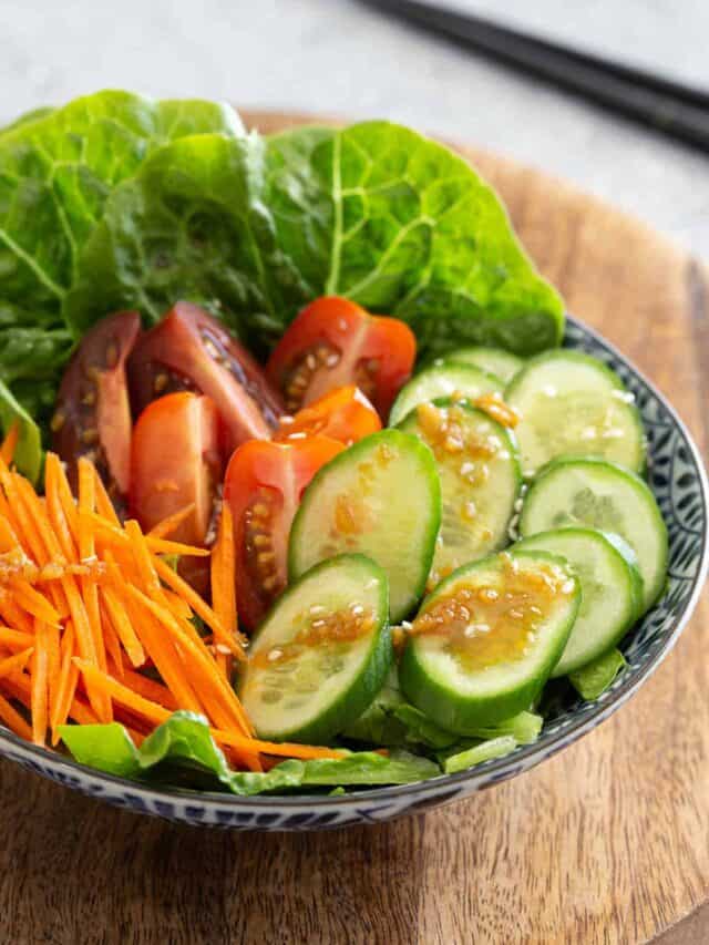 A bowl of salad veggies topped with wafu salad dressing.
