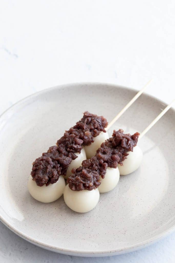 Two sticks of dango covered in anko on a grey plate.