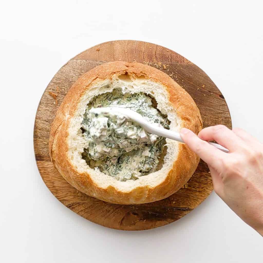 Spooning spinach dip into the hollowed out cob loaf.