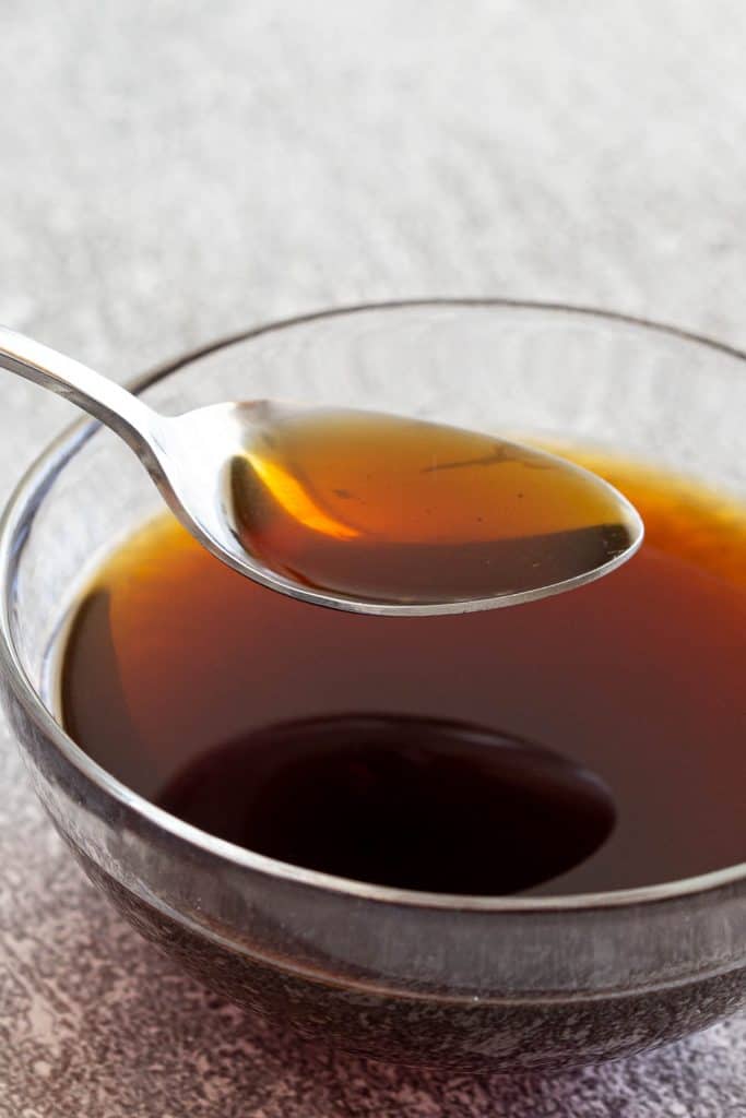 A spoonful of teriyaki sauce above a glass bowl.