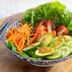 Prepared salad of cucumber, tomato, carrot and lettuce topped with wafu dressing.