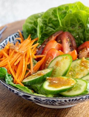 Prepared salad of cucumber, tomato, carrot and lettuce topped with wafu dressing.