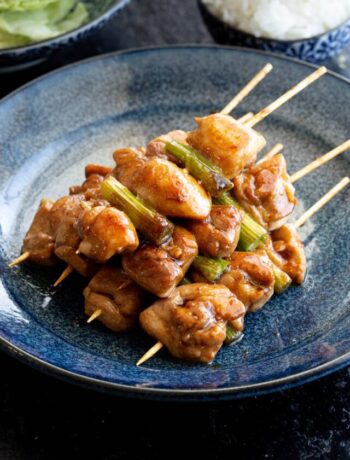 Pile of yakitori chicken skewers on plate with rice and cabbage in background.