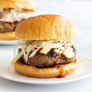 Burger on a white plate dripping with bbq sauce.