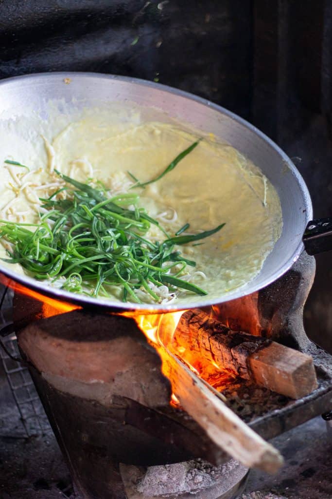 A lao omelette cooking in a large stainless steel wok over a wood fire brazier.