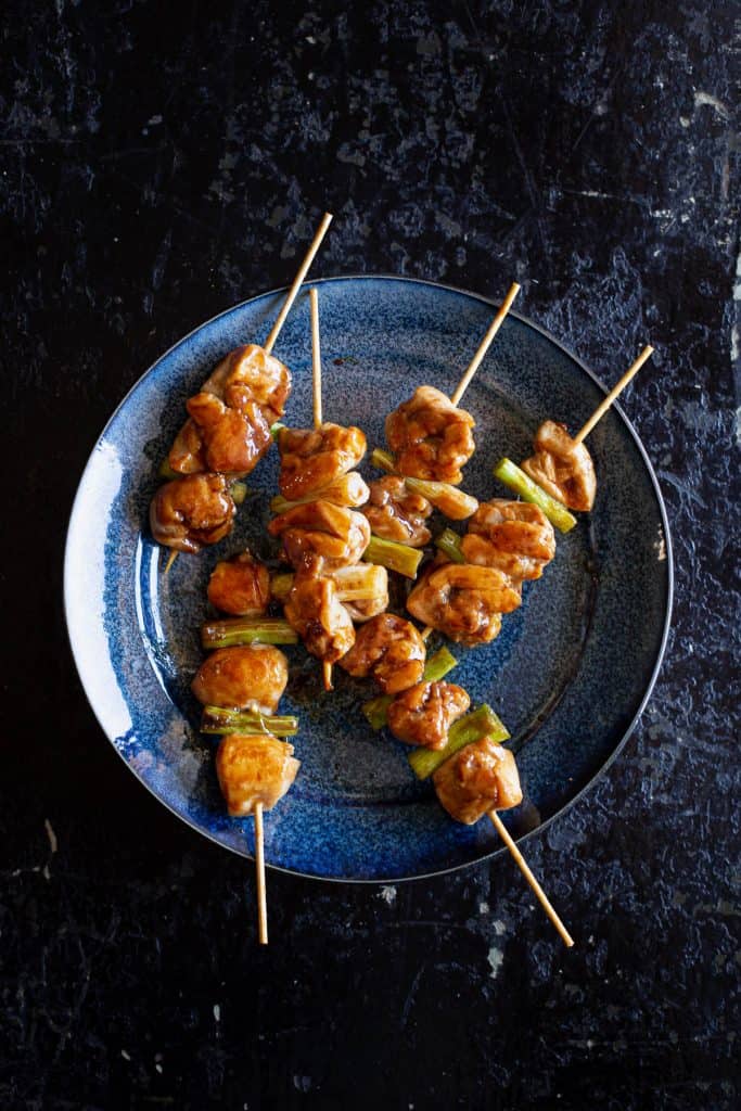 Top view of chicken skewers scattered on a blue plate with dark background.