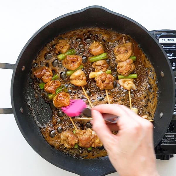 Basting teriyaki sauce over yakitori chicken in a pan.