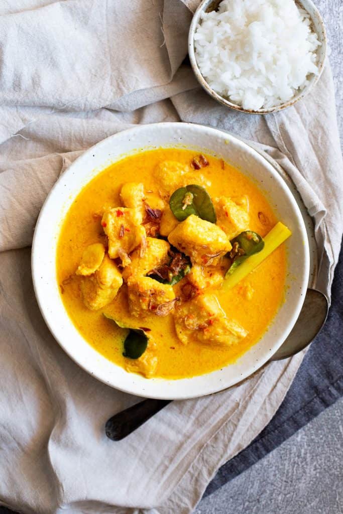 A bowl of bright yellow Indonesian fish curry with fresh lemongrass and kaffir lime leaves.