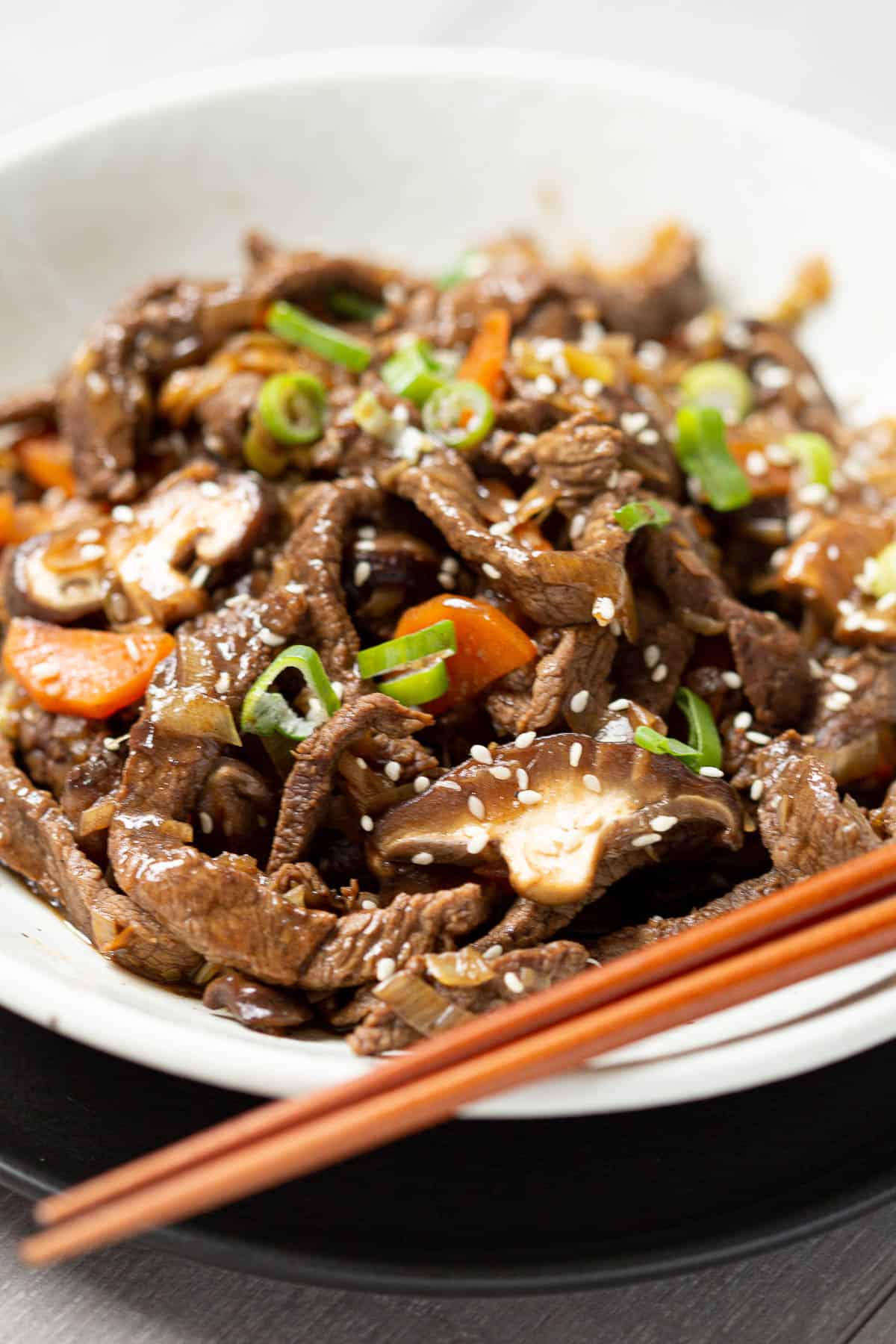 Beef bulgogi cooked with shiitake mushrooms in a bowl next to wooden chopsticks.
