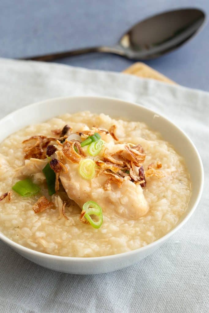 Instant pot chicken congee in a white bowl topped with fried onion and spring onion.