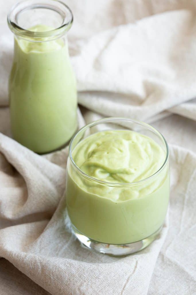 A glass and a bottle filled with green avocado smoothie, sitting on a folded cloth.