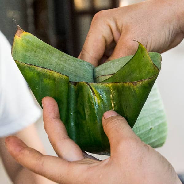 Folding in the first side of the banana leaf wrapper.