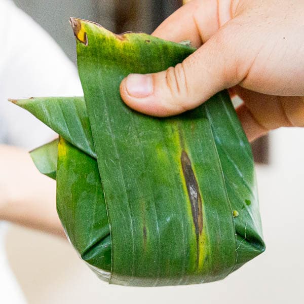 Placing an extra strip of banana leaf around the bottom of the parcel to hold it together.