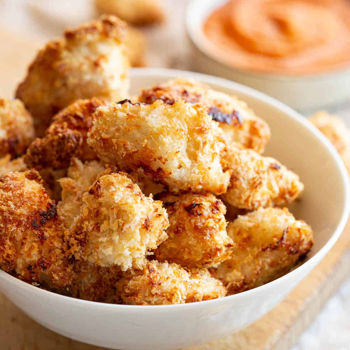 Bowl of crispy air fryer popcorn chicken with dipping sauce in background.