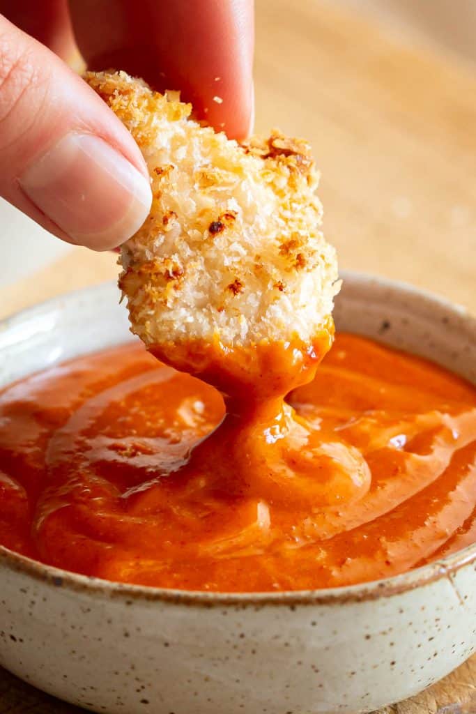 Piece of chicken being dipped into gochujang dipping sauce.