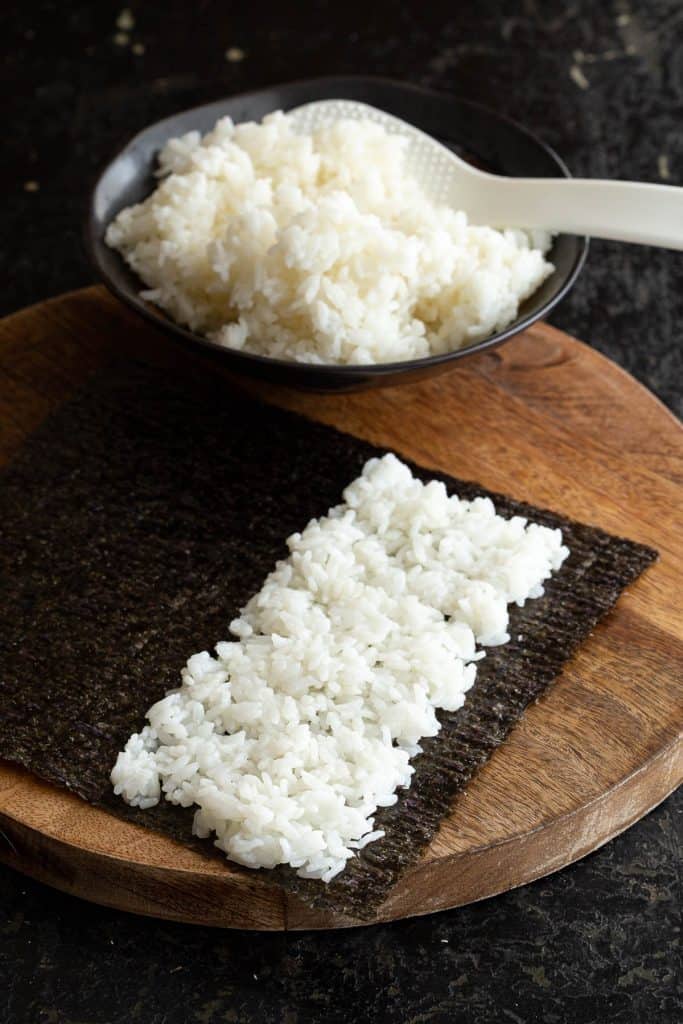 Layering sushi rice onto a nori sheet with rice paddle.
