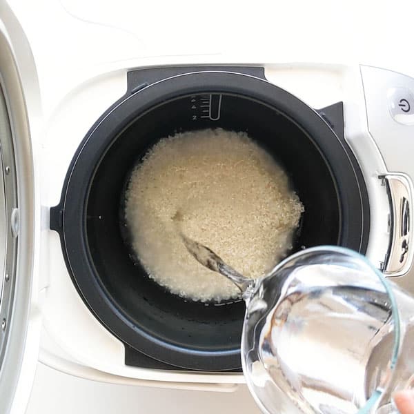 Pouring water over sushi rice in rice cooker.