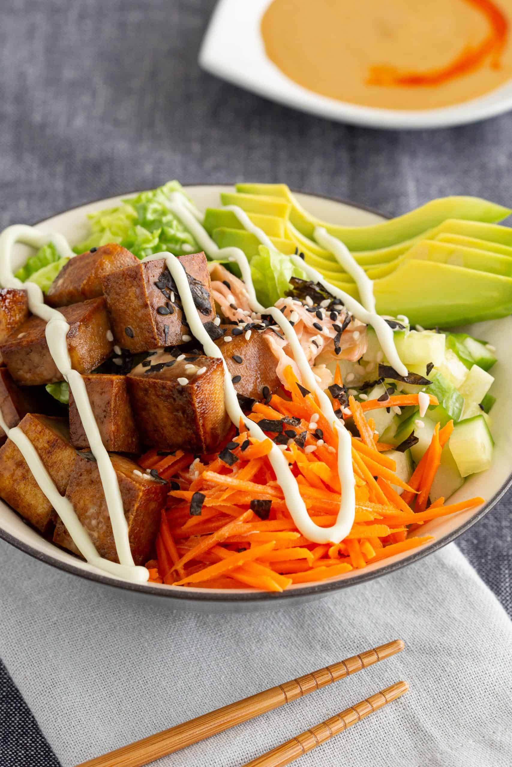 A colourful sushi bowl with tofu and vegetables, next to a bowl of sauce.