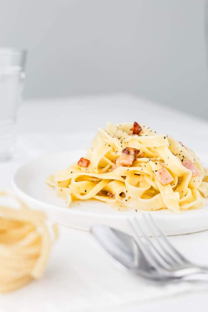 Carbonara on a plate next to a fork and spoon.