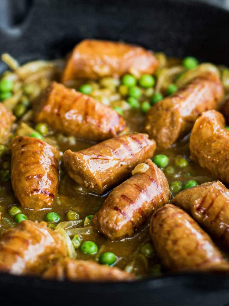 A close up shot of curried sausages cooking in a pan.