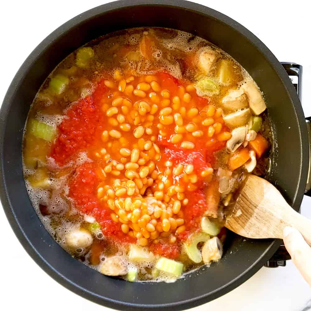 Mixing baked beans and chopped tomatoes through stew.