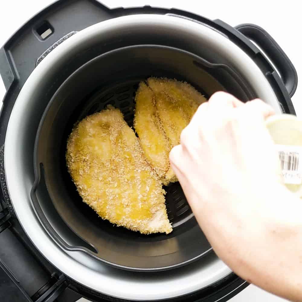 Adding oil to the top of the chicken in the air fryer.