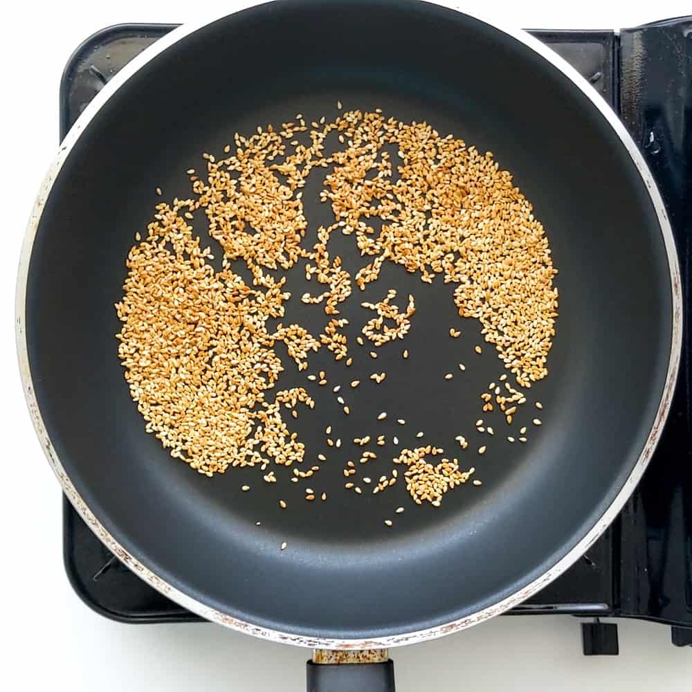 Dry toasting white sesame seeds in a frying pan.