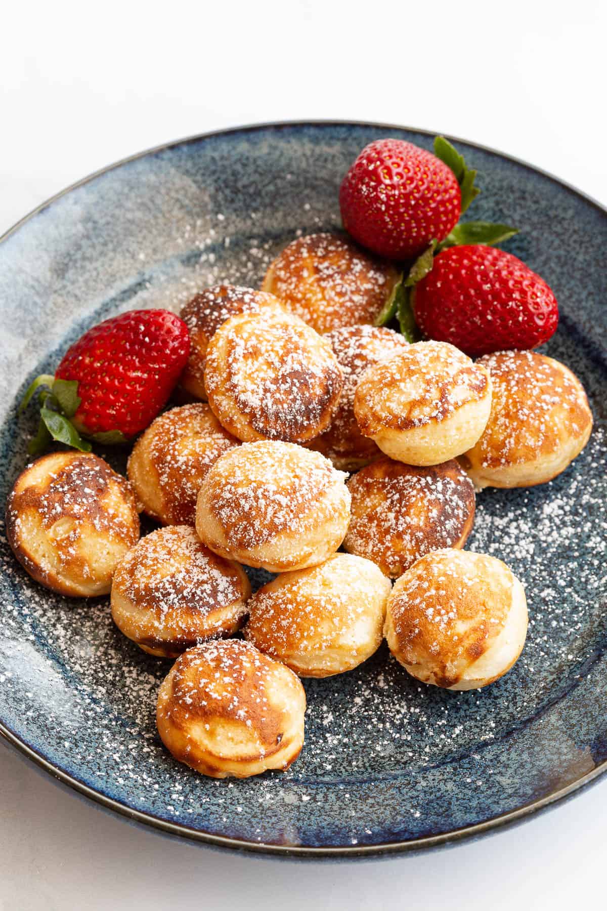 Plate of Dutch mini pancakes with strawberries and powdered sugar.