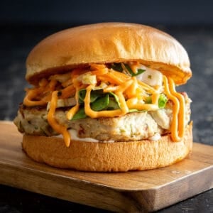 A high stacked Thai chicken burger on wooden board.