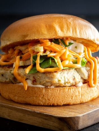 A high stacked Thai chicken burger on wooden board.