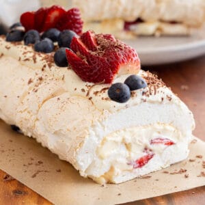 Pavlova roll with berries on a wooden board.