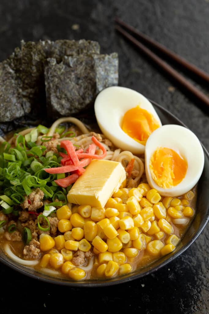 Large bowl of miso ramen topped with corn, eggs, beni shoga and nori.