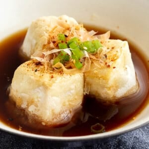 Agedashi tofu in tsuyu sauce in a white bowl.