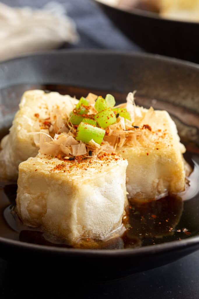 Close up of air fried tofu pieces topped with bonito and spring onion.