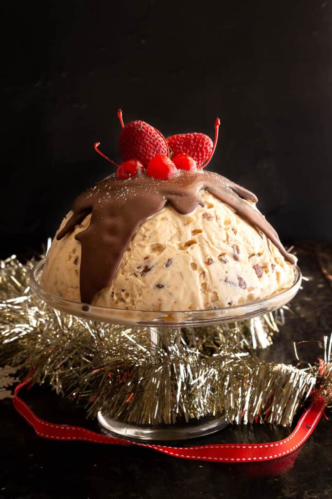 Christmas ice cream pudding on a cake stand surrounded by tinsel.