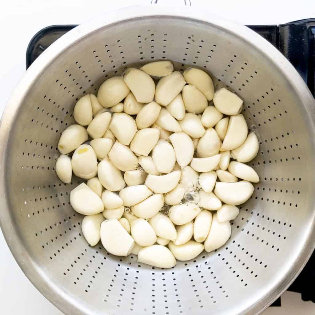 Boiling garlic cloves in a colander.