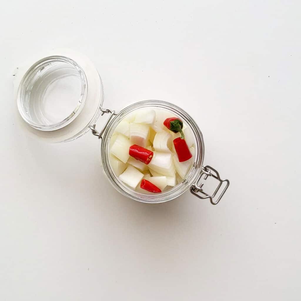 Placing the chopped onion and chilli into a glass jar.