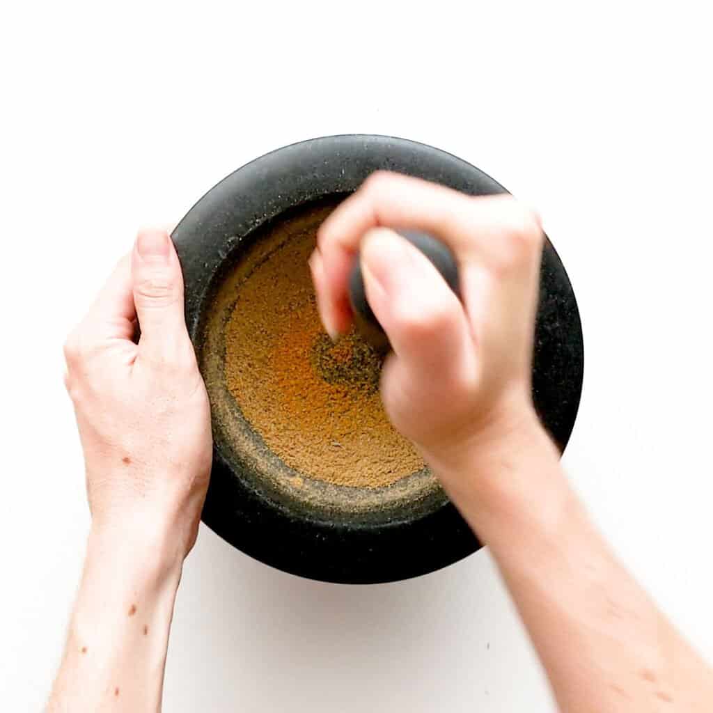 Crushing whole spices in a mortar and pestle.