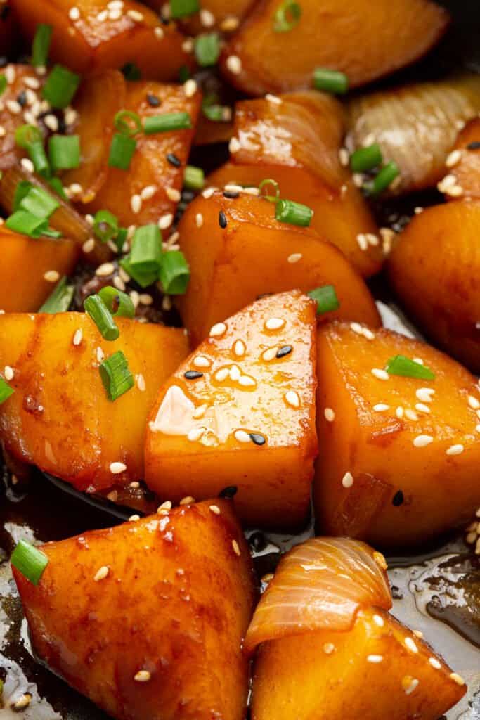 Glossy pieces of braised potato in a frying pan.