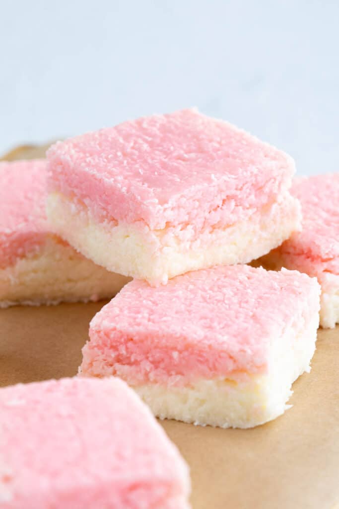 A pink and white coconut slice resting on top of other slices.