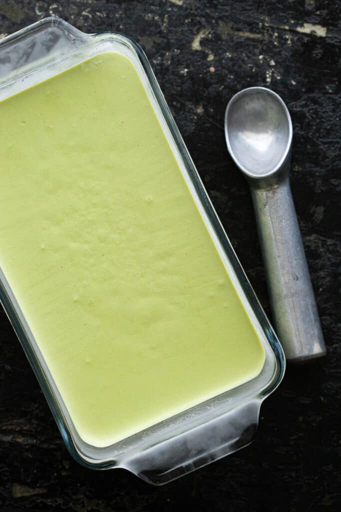 Green tea ice cream in a glass dish with ice cream scoop.