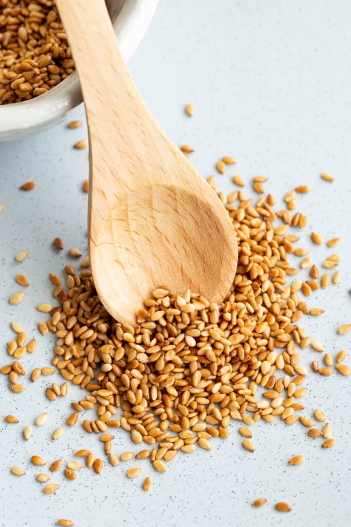 Golden roasted sesame seeds alongside a wooden spoon.