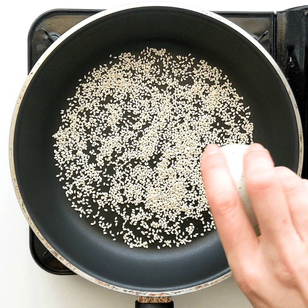 Pouring white sesame seeds into a dry frying pan to toast.
