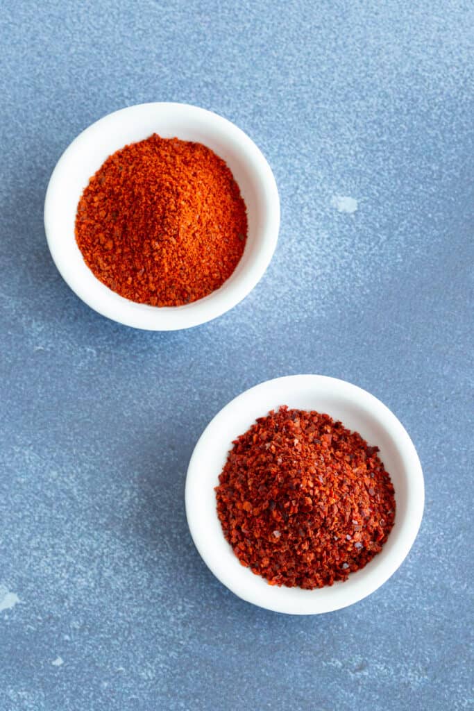 Two white bowls filled with red chilli powder on a blue background.