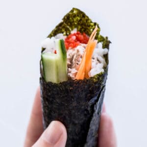 A hand holds up a hand rolled sushi cone.