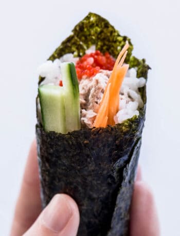 A hand holds up a hand rolled sushi cone.