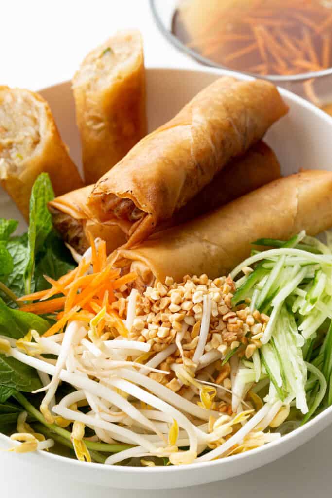 A colourful noodle salad bowl topped with spring rolls and crushed peanuts.