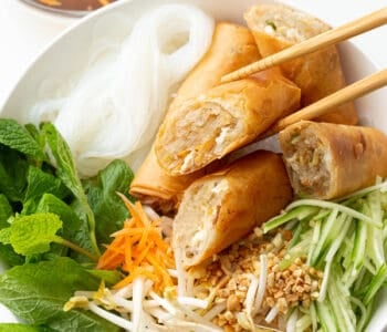 Top down view of bun cha gio with chopsticks holding a sliced spring roll piece to show off the filling.