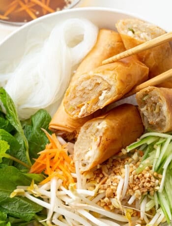 Top down view of bun cha gio with chopsticks holding a sliced spring roll piece to show off the filling.