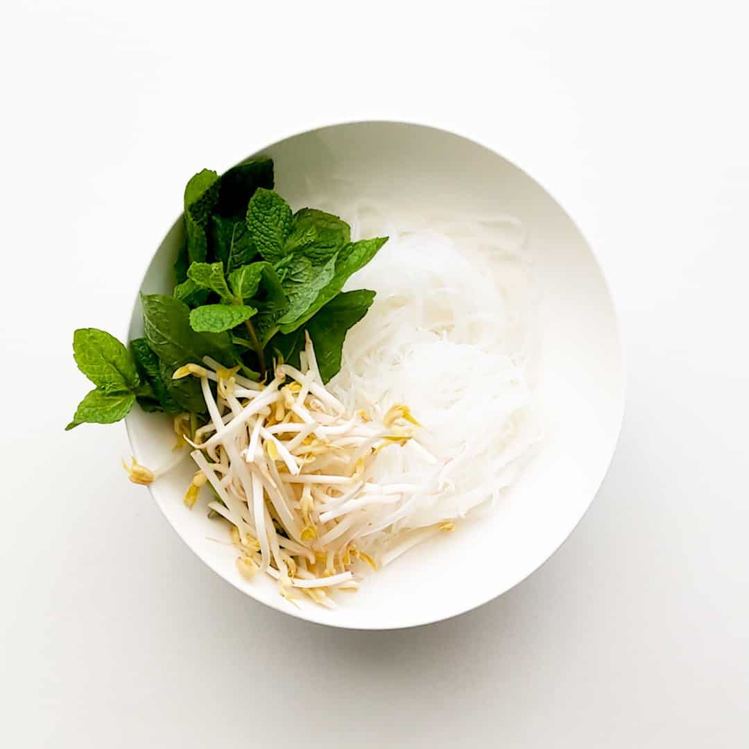 A bowl of vermicelli noodles with mint and bean shoots.